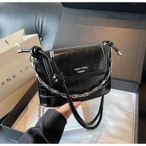 Detail of black glossy crackle leather bucket bag with silver chain and knotted strap