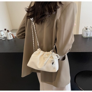 Détail du sac seau plissé crème avec nœud en perles et pendentif cœur sur chaîne argent