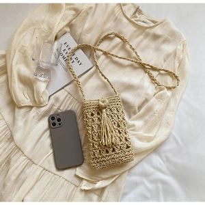 Detailed close-up of handmade woven straw crossbody bag with decorative tassel and strap