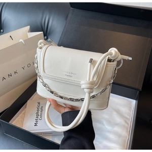 Close-up of cream leather bucket bag featuring silver chain and knotted rope handle