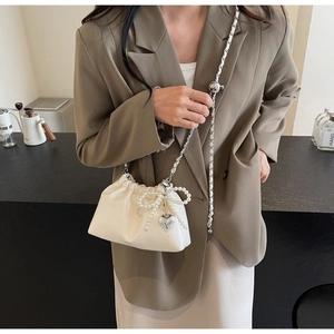 Détail du sac seau crème avec nœud en perles, pendentif cœur et bandoulière chaîne réglable