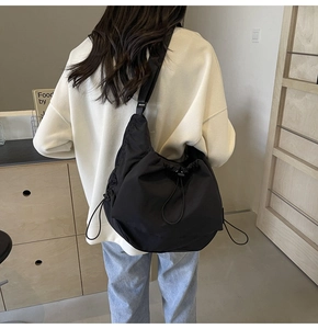 Model view of a black nylon crossbody tote bag with wide strap and drawstring detail