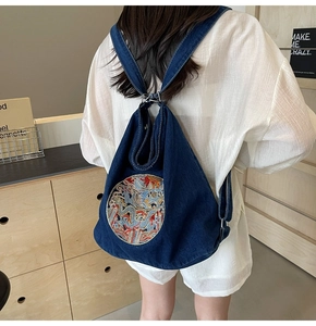 Detailed close-up of a dark blue denim backpack with a dragon embroidery on a model