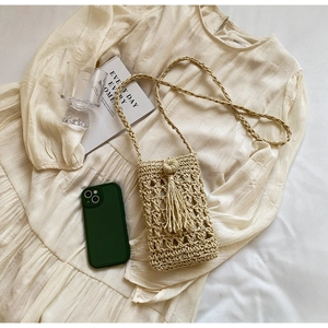 Detail of hand-woven straw phone bag with tassel charm on a neutral textured background