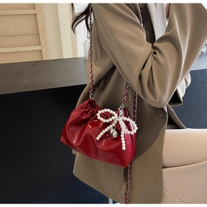Détail du sac seau en cuir verni rouge avec nœud en perles et pendentif coeur