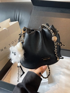 Elegant black drawstring bucket bag with gold chain strap and fuzzy monster charm