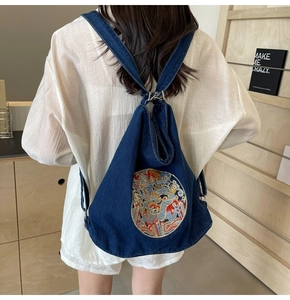 Detailed view of the dragon embroidery on dark blue denim backpack with drawstring closure