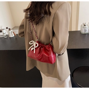 Détail d'un sac seau rouge brillant avec cordon de serrage et breloque nœud en perles