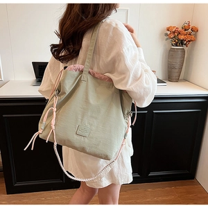 Close-up of light green nylon tote bag featuring pink drawstring and leather label
