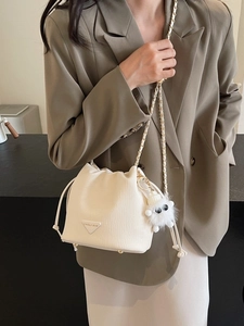 Chic off-white drawstring bucket bag with gold chain strap and plush monster charm