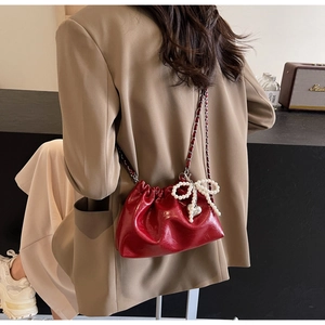 Détail du sac seau en cuir verni rouge avec bandoulière chaîne et charm nœud perlé