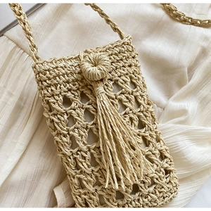 Detail of woven straw crossbody bag with fringe tassel on neutral fabric background