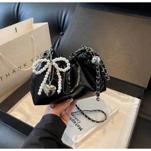 Détail du sac seau noir brillant avec nœud en perles et breloque cœur argentée