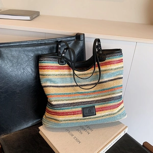 Colorful woven tote bag with horizontal stripes and black leather handles shown from a side view