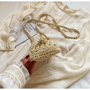 Detailed close-up of handmade woven mini straw bag with tassel detail and braided strap