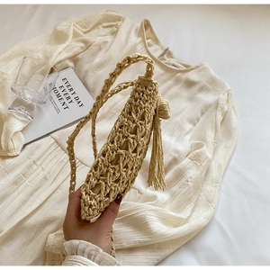 Detailed side view of handmade straw shoulder bag with elegant tassel and woven texture