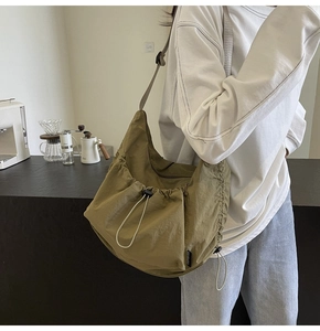 Olive green nylon tote bag with drawstring detail shown in a casual lifestyle setting