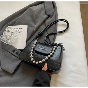 Close-up of black crocodile pattern bag with silver bead chain and metal logo detail