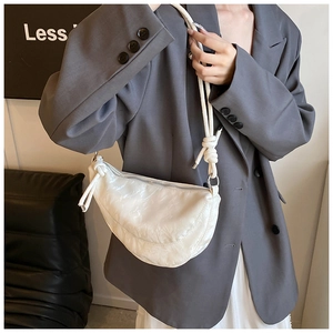 Detail of white half-moon bag featuring pleated texture and chunky rope strap knots