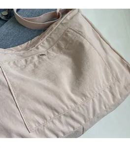Detail of light pink nylon bag showing front pocket with metal snap and stitching