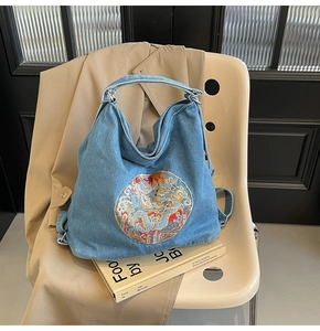 Detail of light blue denim tote bag with colorful ethnic dragon embroidery on the front