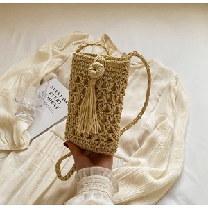Macro detail of hand-woven straw phone bag with tassel and textured stitch pattern