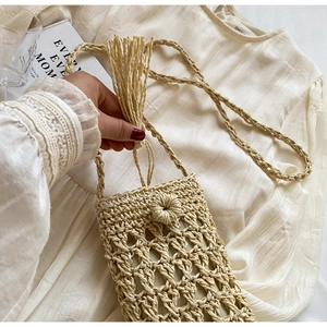 Detail of woven straw phone bag featuring long fringe tassels and artisanal texture