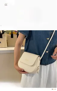 Detail view of cream saddle bag with gold logo on denim jacket with slim strap