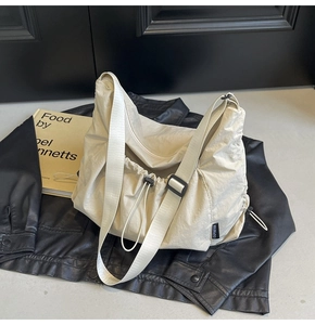 Detail of cream nylon crossbody bag with drawstring closure and brand label on leather