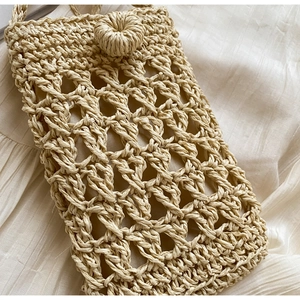 Detail of hand-woven straw crossbody bag with hollow diamond pattern and button closure