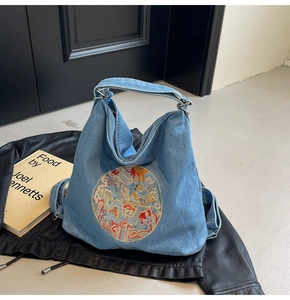 Detail view of denim tote bag featuring intricate colorful dragon embroidery and texture