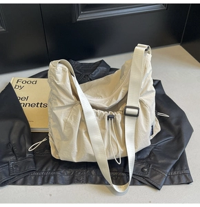 Detail of cream nylon crossbody hobo bag with drawstring texture and adjustable shoulder strap