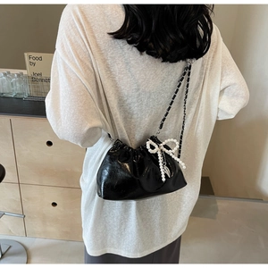 Détail du sac seau noir brillant avec pendentif nœud perlé et bandoulière en chaîne