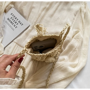 Detail view of woven straw crossbody bag showing interior storage for phone and lipstick
