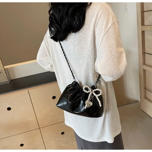 Détail d'un sac seau noir brillant avec nœud perlé et pendentif cœur sur le mannequin