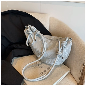 Detail of light grey pleated crescent bag with knotted shoulder strap on sofa