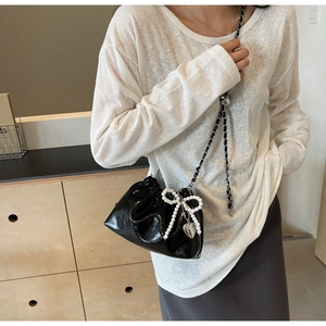 Détail du sac seau noir avec nœud en perles, pendentif cœur et bandoulière chaîne