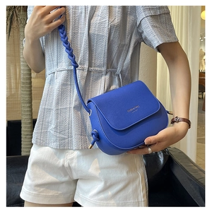 Detail of blue saddle bag with braided shoulder strap and gold stamped fashion logo