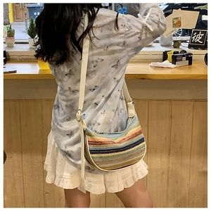Close-up of colorful striped knit half-moon bag with white leather strap and metal buckle