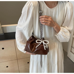 Détail d'un sac seau marron avec nœud en perles et breloque cœur sur chaîne