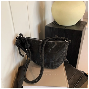 Detailed view of black pleated crescent bag with thick knotted shoulder strap on books