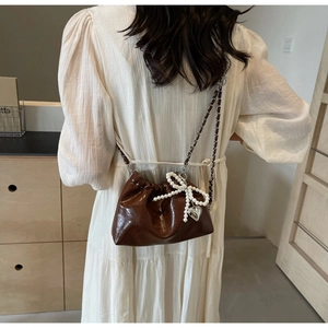 Détail du sac seau marron foncé avec breloque nœud en perles et bandoulière chaîne