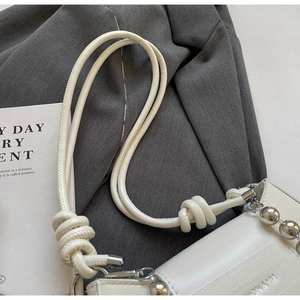Close-up of white glossy shoulder bag with knot strap and silver ball chain detail