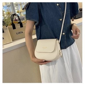 Detail of a creamy white PU leather saddle bag with gold lettering and knot strap detail