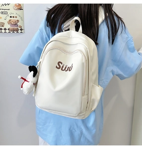 Detailed view of white nylon backpack with brown Sūjū logo and cute puppy plush charm