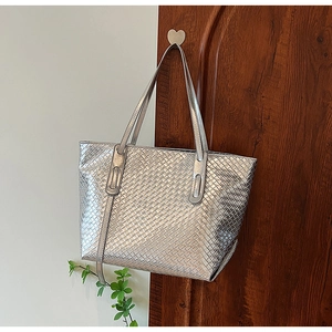 Detail of silver woven tote bag showing metallic texture hanging on a wooden door hook