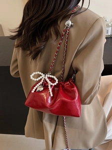 Sac seau en cuir verni rouge avec chaîne et breloque nœud en perles porté par mannequin