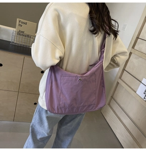 Detail of a purple nylon crossbody bag with front snap pocket on a model's shoulder