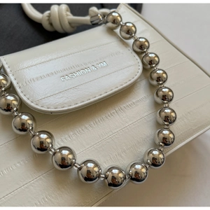 Close-up of white embossed crocodile texture bag with chunky silver bead chain detail