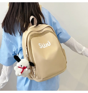 Detail of cream nylon backpack with plush charm and brand logo worn by a model